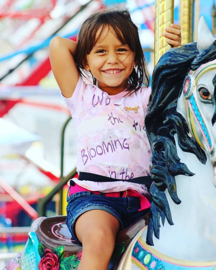 Young child smiling and riding a carousel horse.