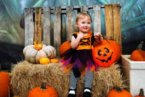 Little girl in costume sitting on hay surrounded by pumpkins