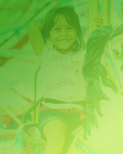 A little girl smiling on a ride with a green overlay on the image